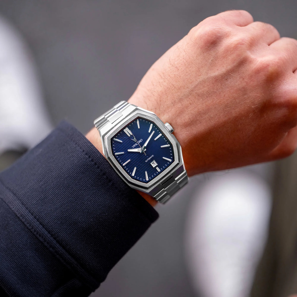 Close-up of a wrist wearing a silver watch with a blue face against a blurred background
