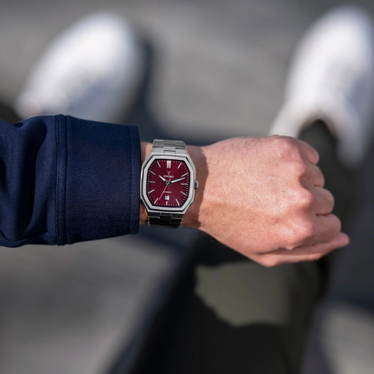 Person wearing a watch with a red face and silver case on a blurred background