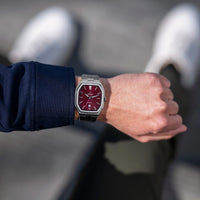 Person wearing a watch with a red face and silver case on a blurred background