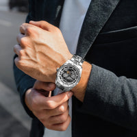 Person wearing a silver wristwatch with a detailed face, dressed in a dark suit.