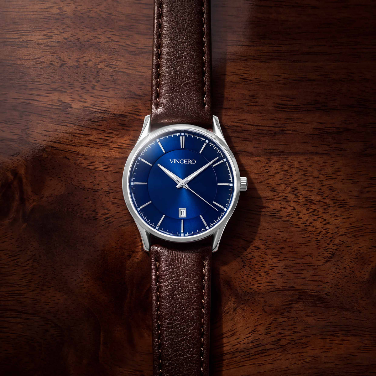 A VINCERO wristwatch with a blue dial and silver case, fitted with a brown leather strap, photographed from above on a dark wood surface.