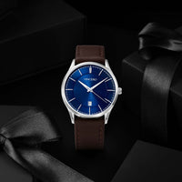 A VINCERO wristwatch with a blue dial and brown leather strap, presented on a dark background with black gift boxes and ribbons.