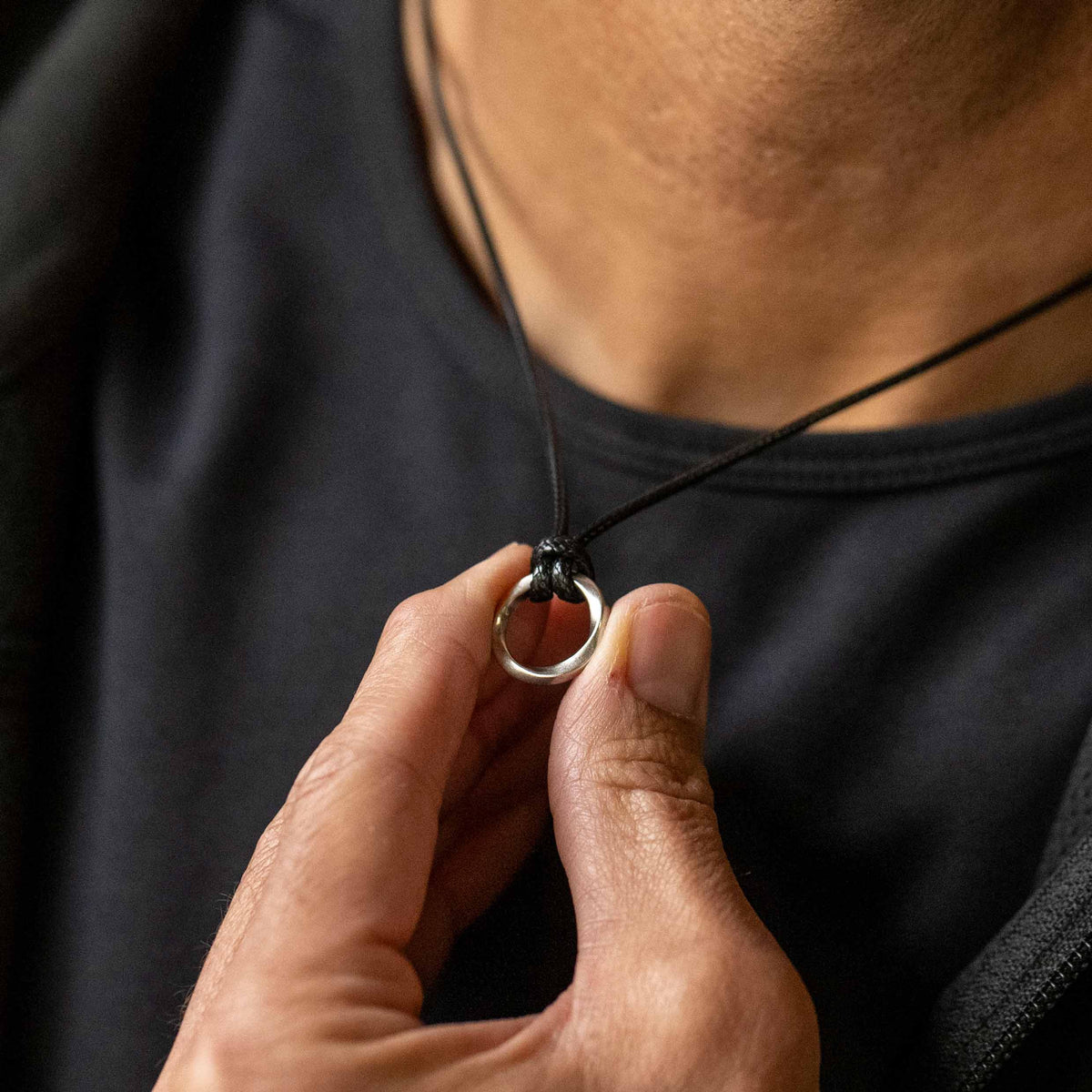 A sterling silver amulet pendant with a silver curb chain necklace and a black waxed cord.