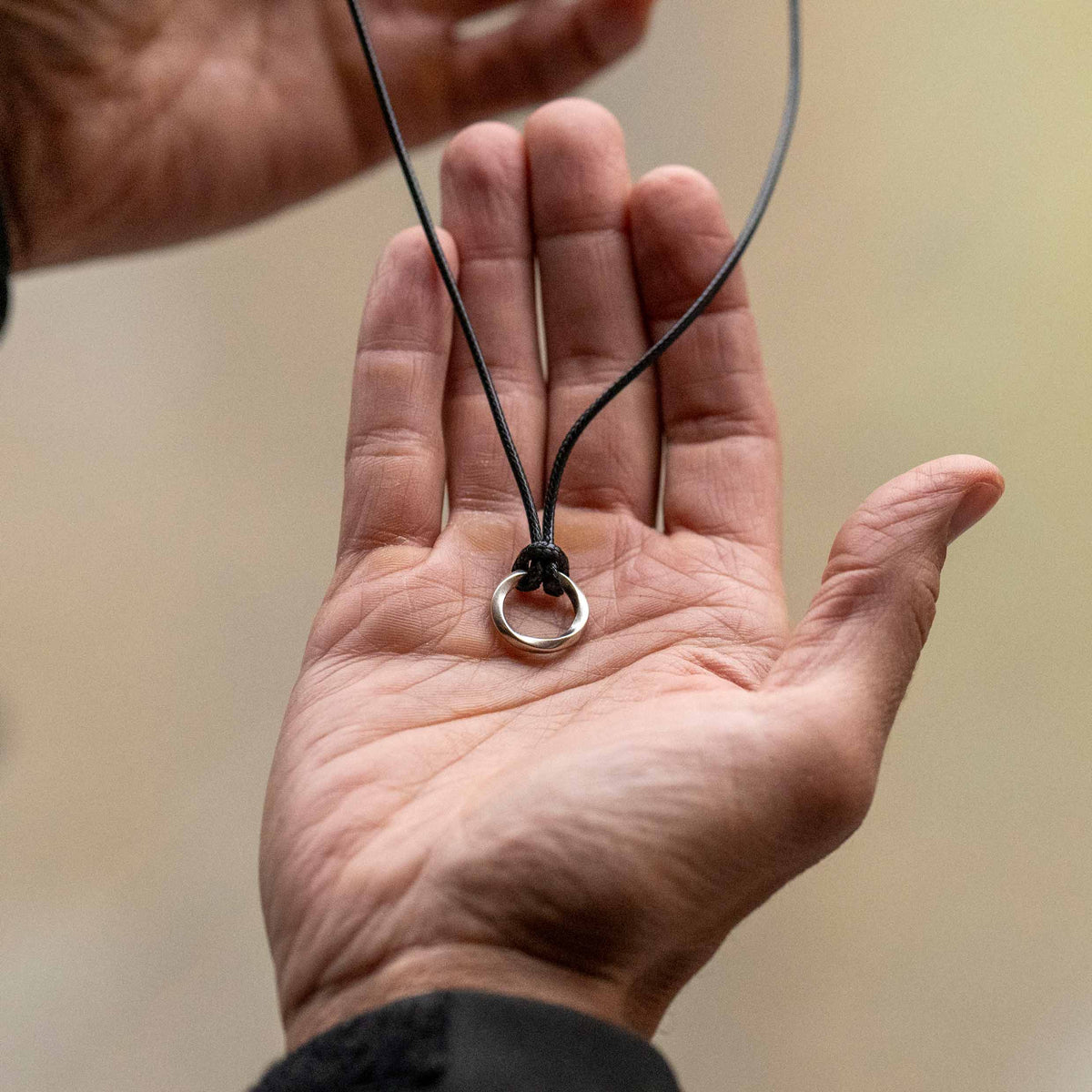 A sterling silver amulet pendant with a silver curb chain necklace and a black waxed cord.