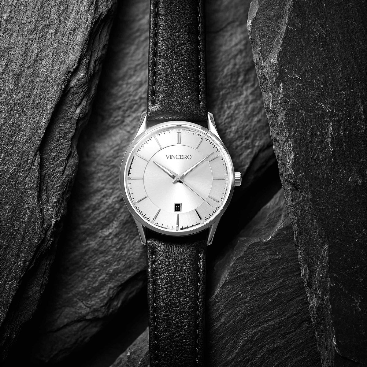 A VINCRO wristwatch with a silver-toned dial and a black leather strap, presented on a dark textured slate background.