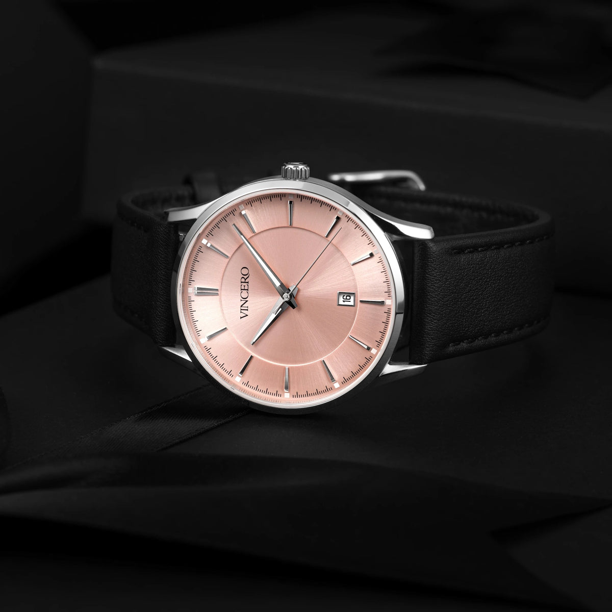 Luxury watch with a pink dial and black strap on a dark background