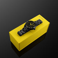 Black wristwatch on a yellow box with 'Vince' brand name against a dark background