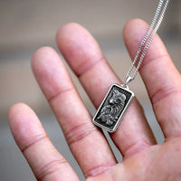 Silver pendant with intricate design held in a hand against a blurred background