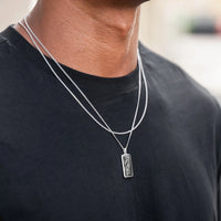 Silver necklace with a pendant on a person wearing a black shirt.