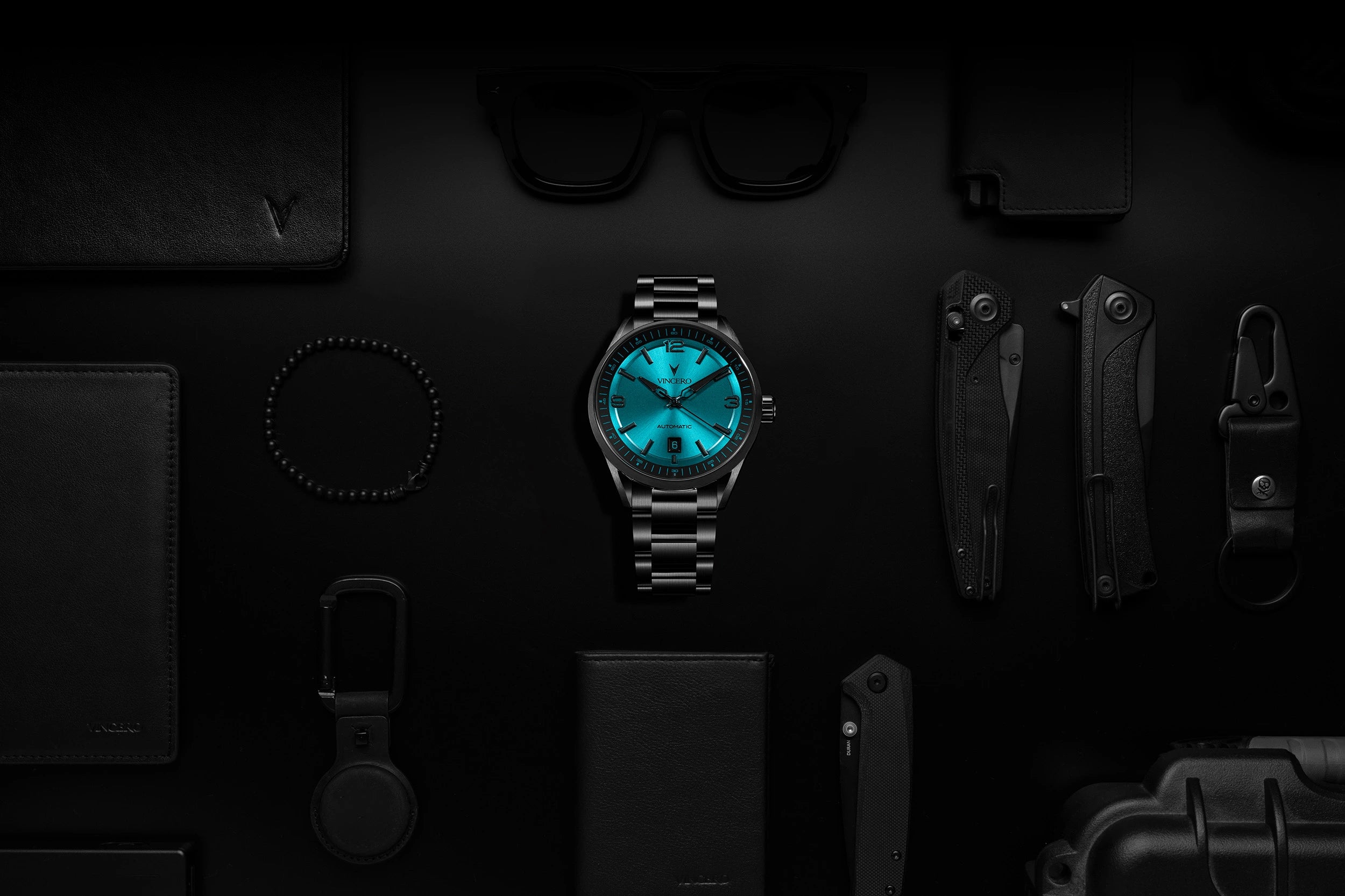 Watch with blue face and silver strap on a dark surface with various items