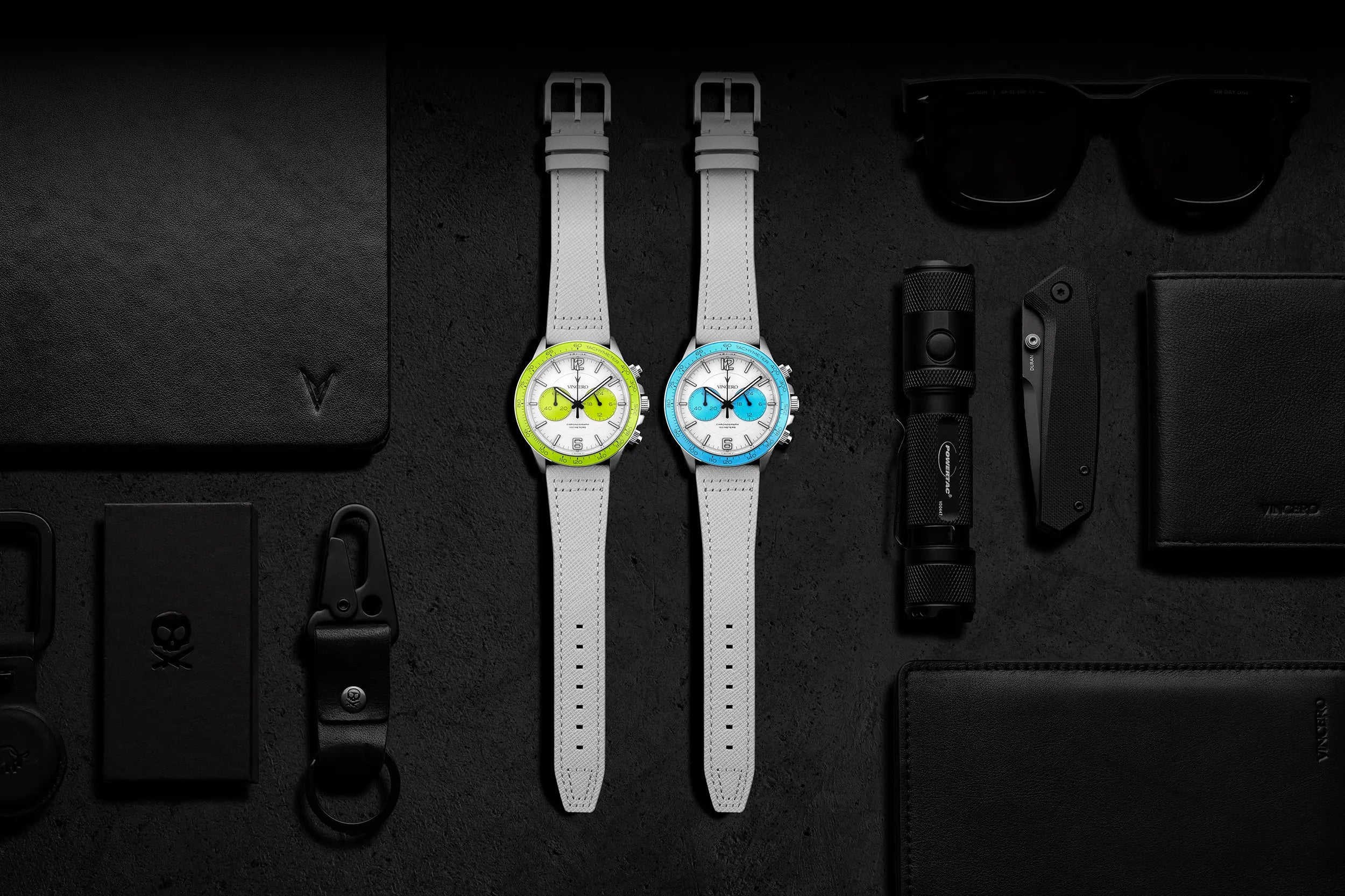 Two watches with colorful faces on a dark surface with various items.