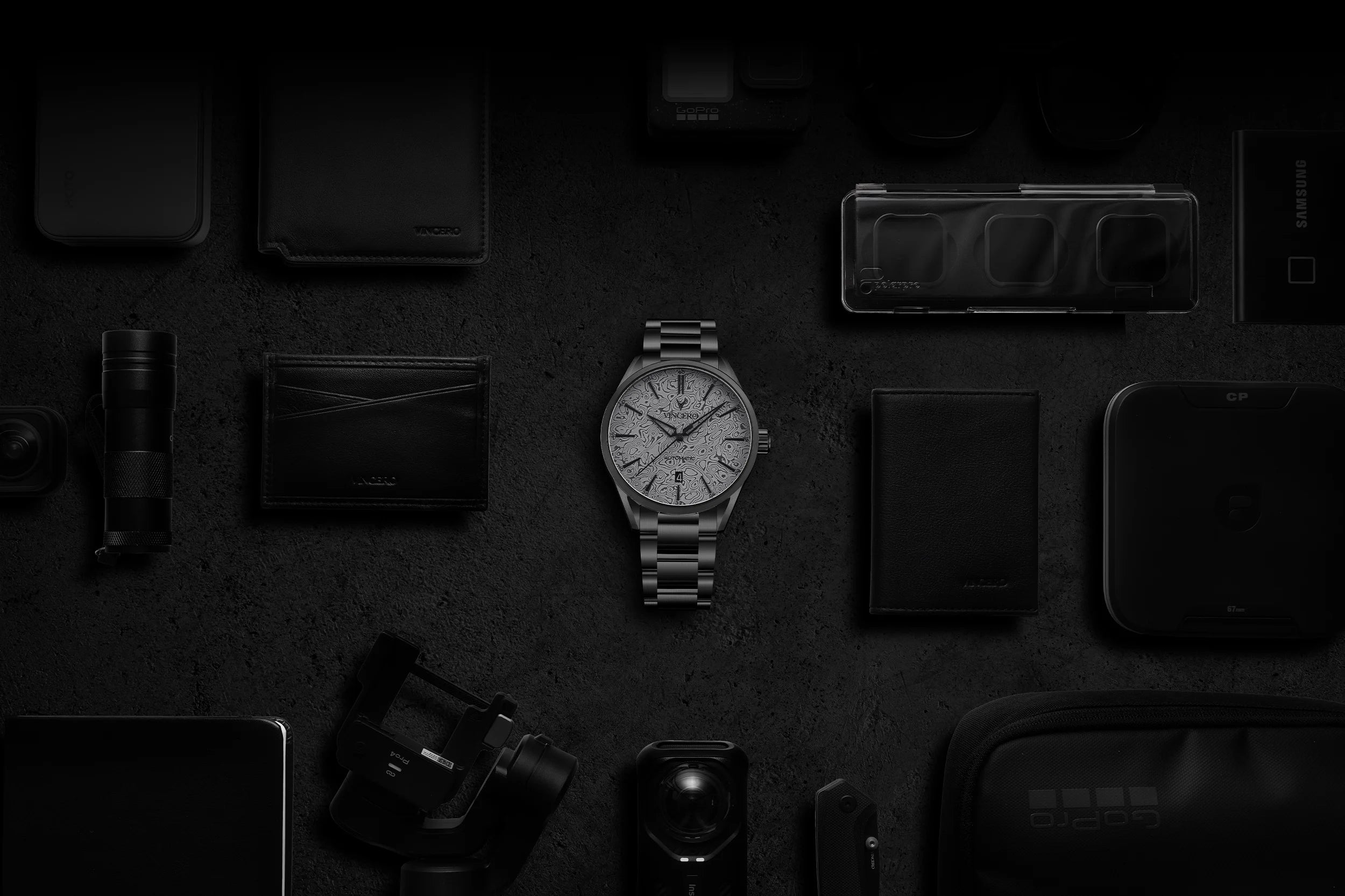 Collection of black leather items including a wallet, phone case, and watch on a dark surface.