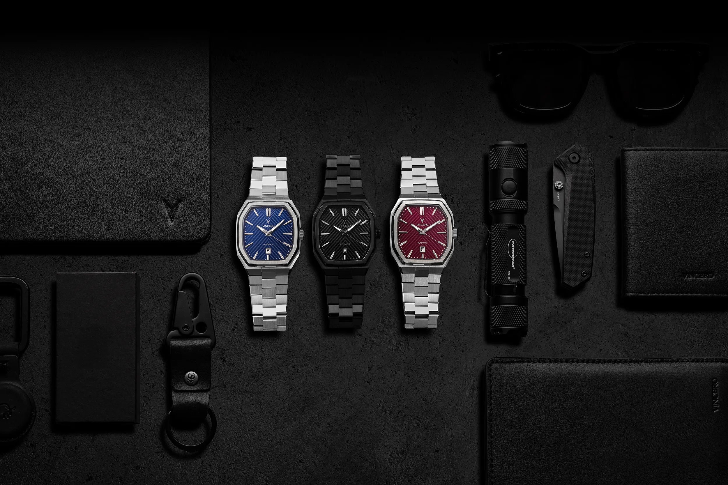 Three watches displayed on a dark surface with various items around.