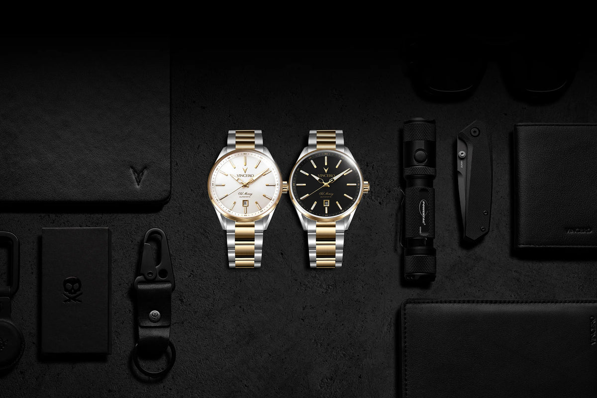 Two luxury wristwatches with two-tone metal bracelets are displayed on a dark textured surface, surrounded by black leather accessories including wallets, a keychain, and a cardholder. One watch has a white dial and the other has a black dial.