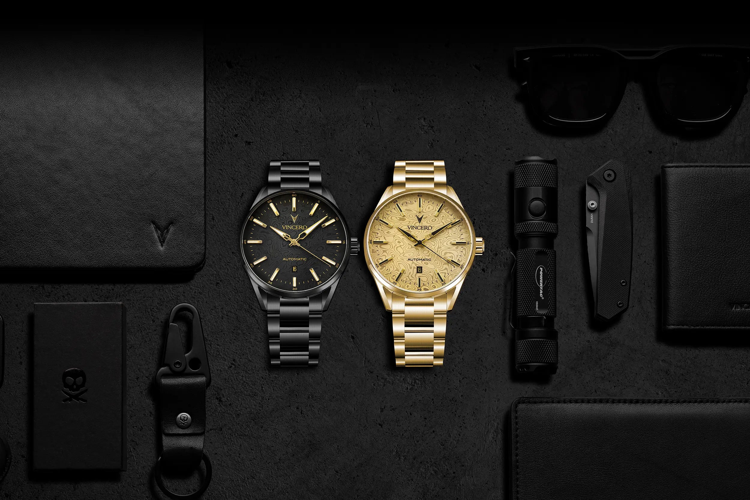 Two men's analog wristwatches are displayed on a dark textured background with matching accessories. The watch on the left has a black case and black dial with gold-tone indices, and the watch on the right has a gold case and gold dial.