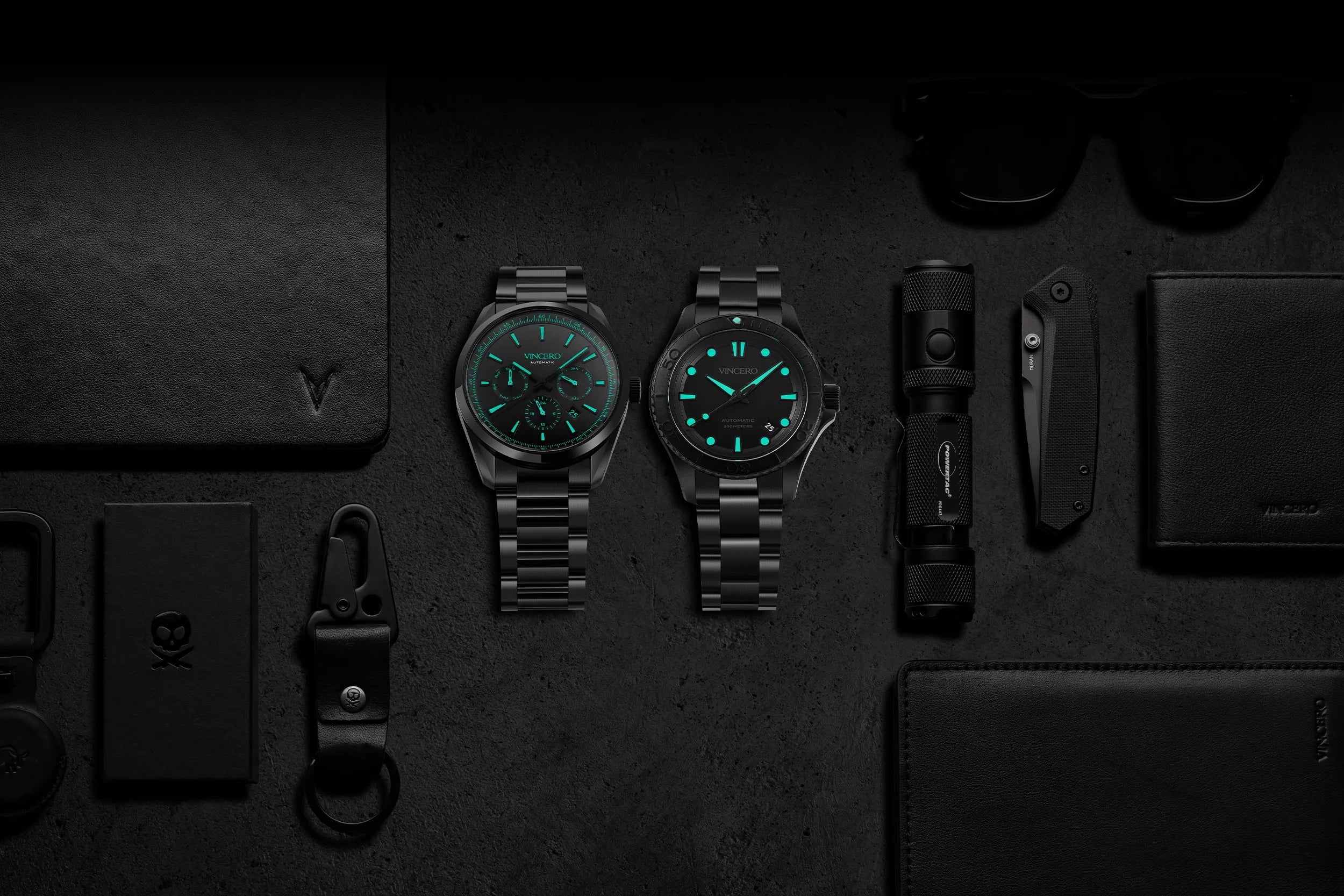 Two watches with green faces on a dark surface with various items.