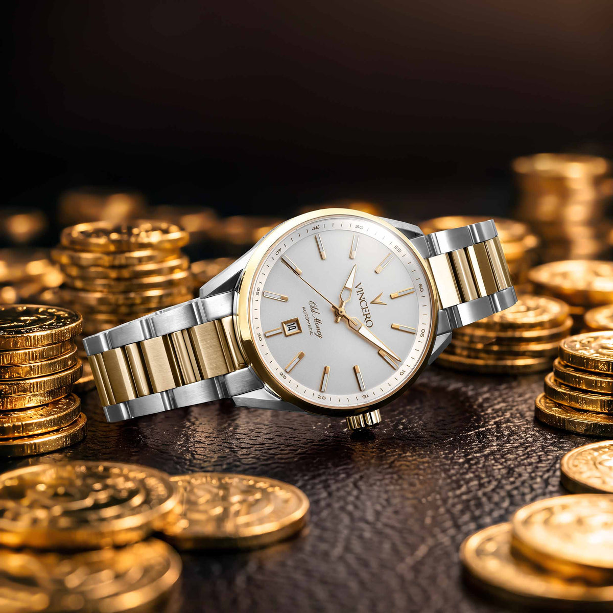 A wristwatch with a silver and gold two-tone metal bracelet, a white dial, and gold accents, styled on a dark textured surface surrounded by stacks of gold coins.