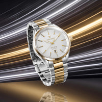 A two-tone stainless steel and gold wristwatch with a white dial, shown floating against a dynamic metallic background with gold and silver streaks.