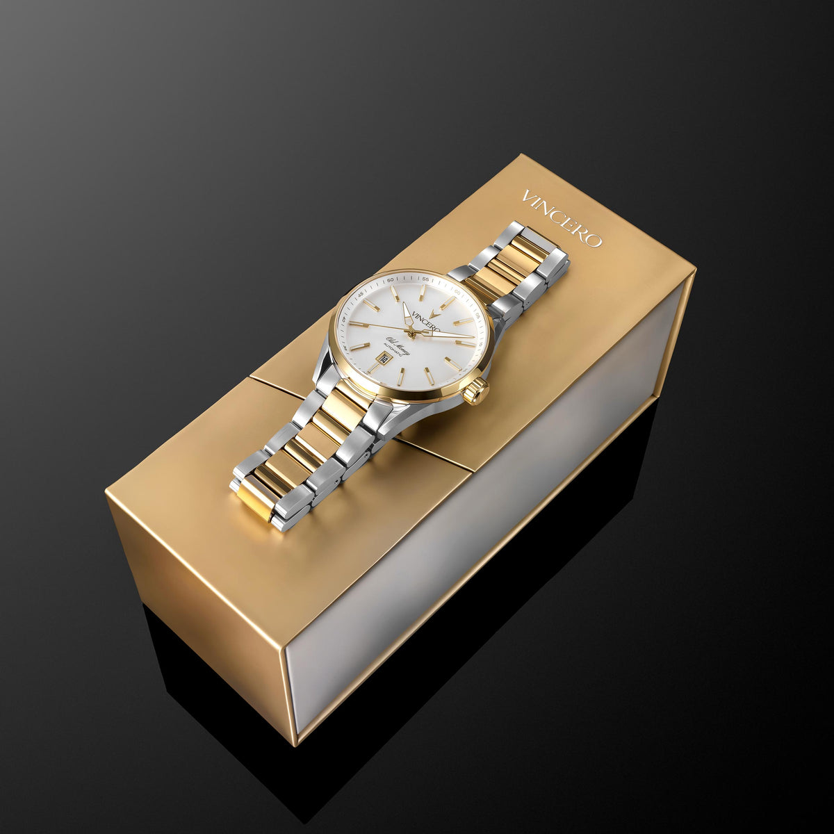 A two-tone stainless steel and gold Vinciero wristwatch with a white dial, resting diagonally on its metallic gold presentation box against a dark reflective background.