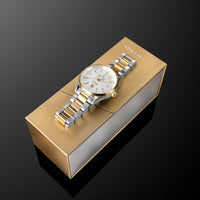 A two-tone stainless steel and gold Vinciero wristwatch with a white dial, resting diagonally on its metallic gold presentation box against a dark reflective background.