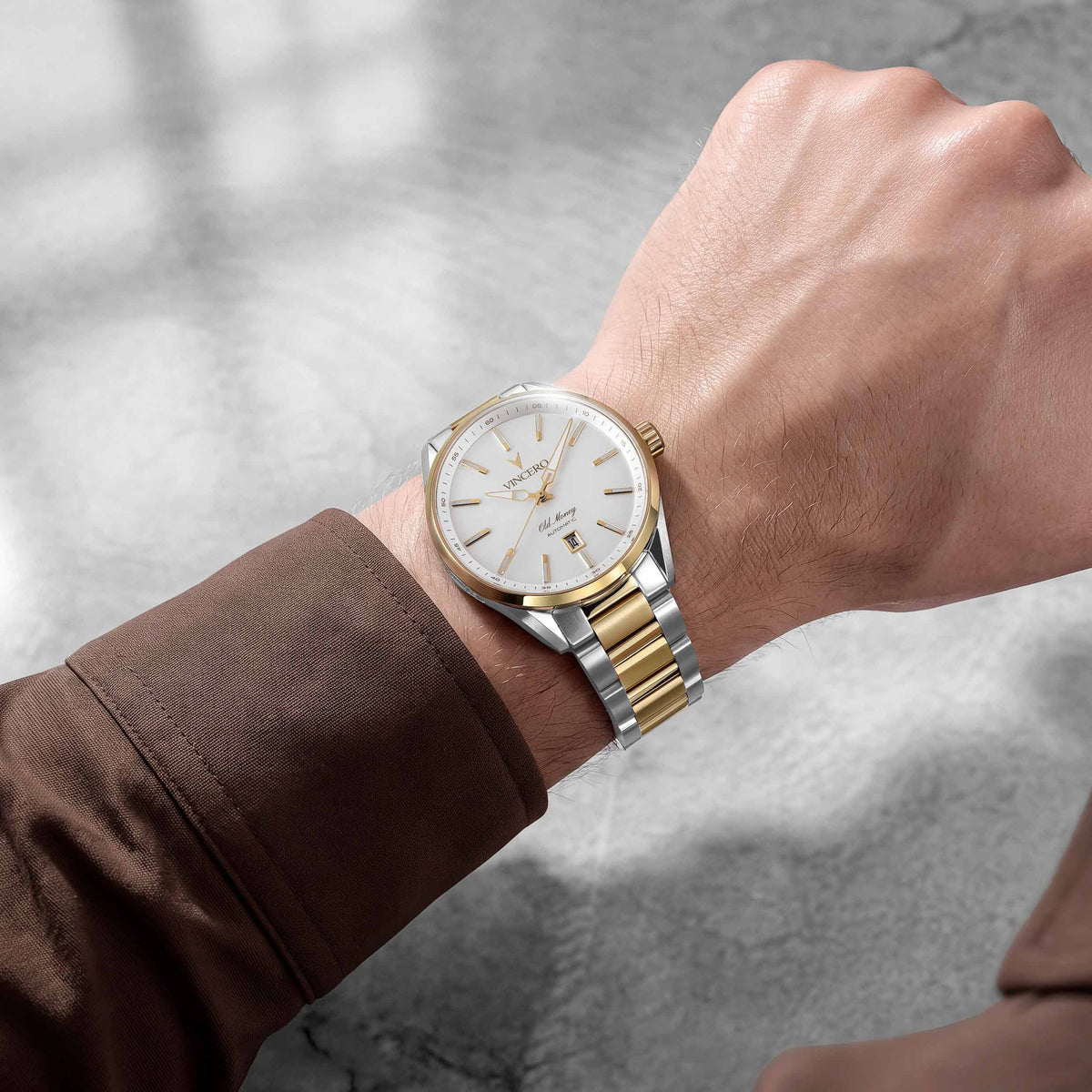 A two-tone stainless steel and gold wristwatch with a white dial, worn on a person's wrist. The watch features a gold-tone bezel, silver-tone case, and a gold-and-silver link bracelet.