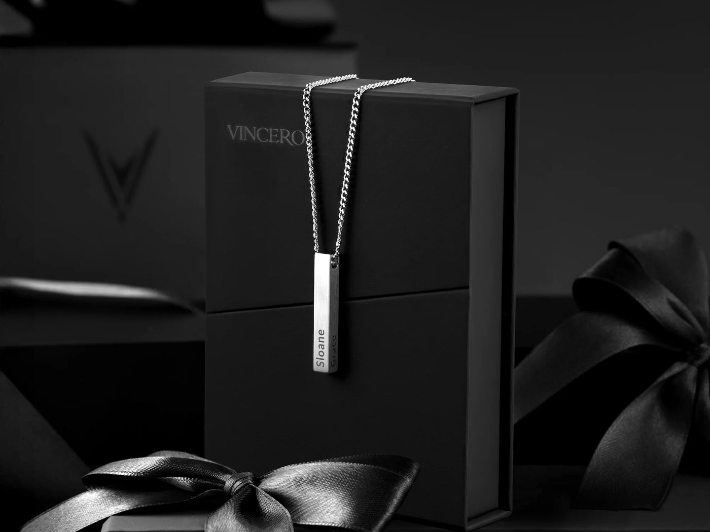 Silver necklace with a pendant on a black box with 'Vincero' branding, surrounded by dark ribbons.