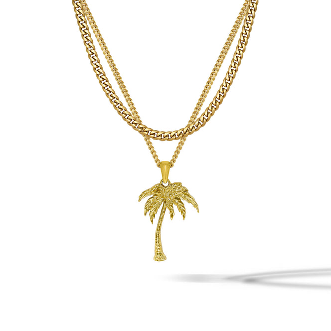 A gold-toned double-strand necklace featuring a curb chain and a thinner chain with a detailed palm tree pendant, displayed on a clean white background with a soft shadow.