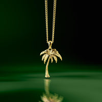 Gold palm tree pendant suspended over green water. A pendant necklace for men. 
