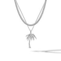 A silver-toned necklace featuring a double-strand chain design, with a curb chain on the top layer and a delicate chain on the bottom layer. Hanging from the bottom of the chain is a palm tree pendant adorned with small clear stones, set against a clean white background with a soft shadow.
