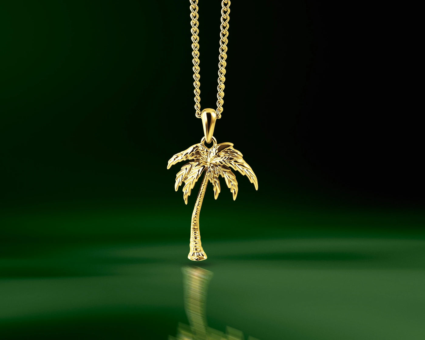 A gold pendant necklace featuring a detailed palm tree charm on a matching chain, set against a dark green reflective background.