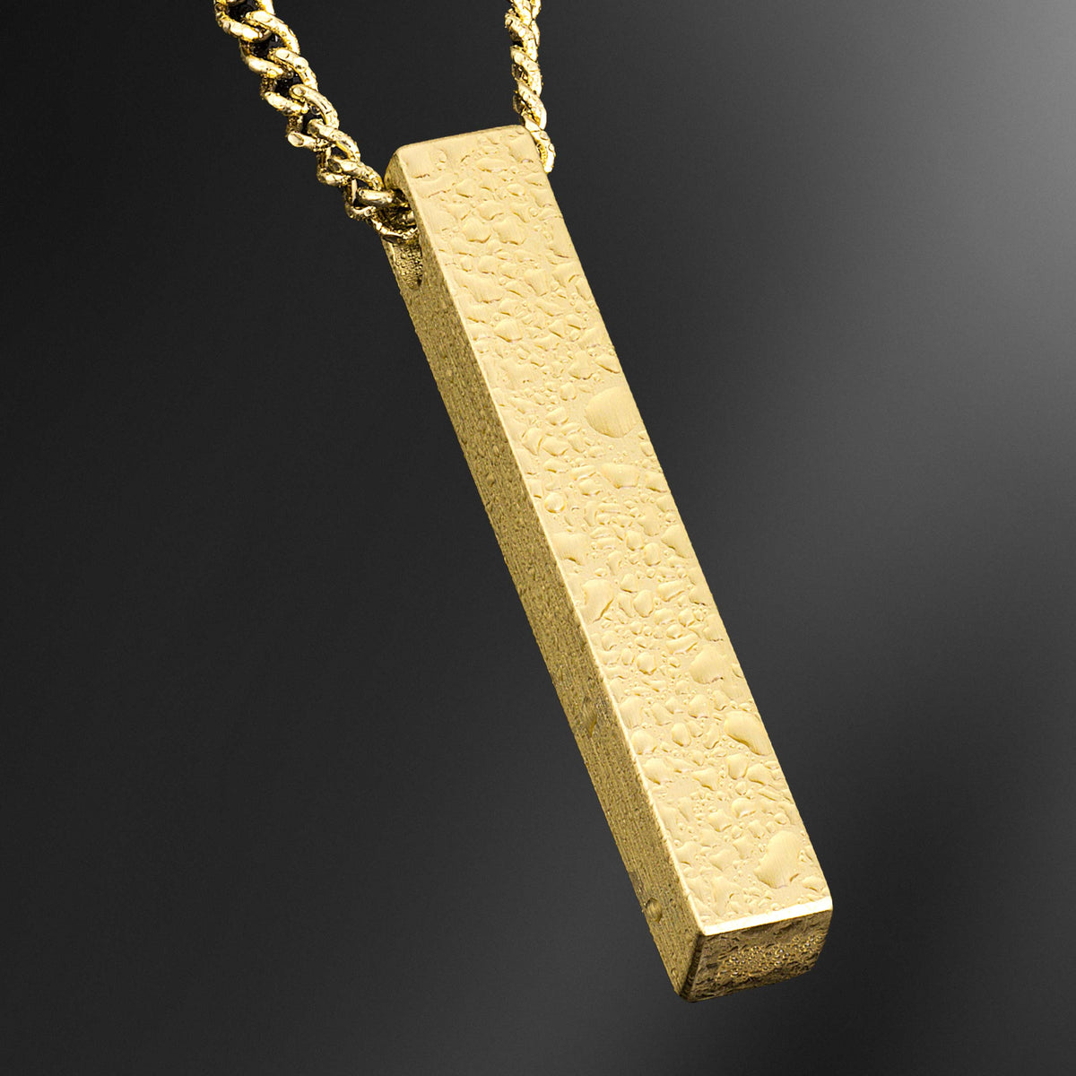 Gold rectangular pendant on a chain against a dark background