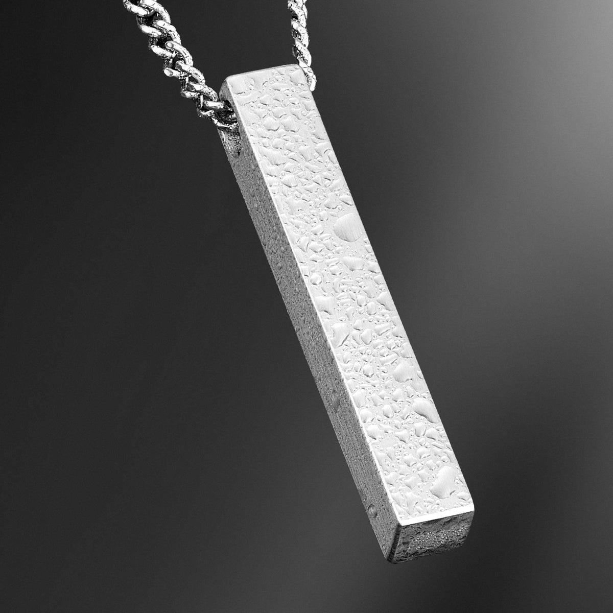 Textured rectangular pendant on a chain against a dark background