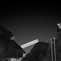 Barbell between two rocky cliffs with a chain hanging from one end, black and white photo