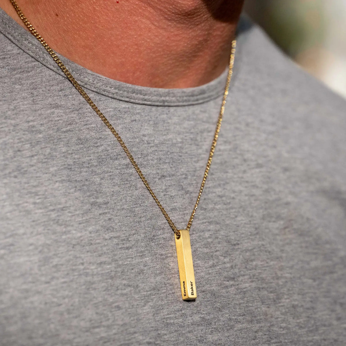 Gold necklace with a vertical pendant on a gray shirt