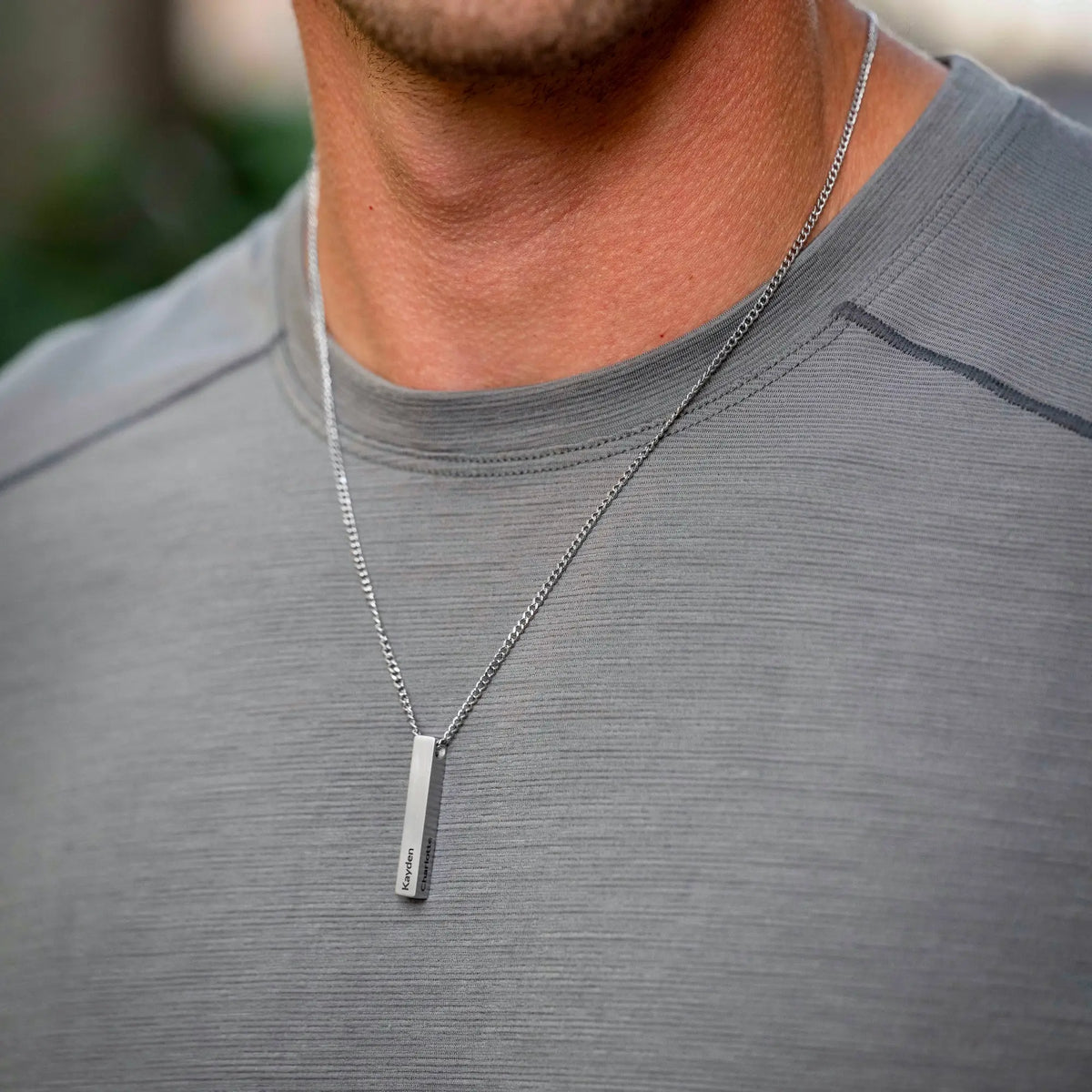 Man wearing a silver necklace with a vertical pendant on a blurred background