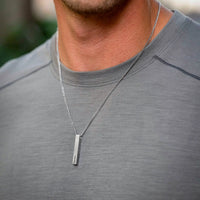 Man wearing a silver necklace with a vertical pendant on a blurred background