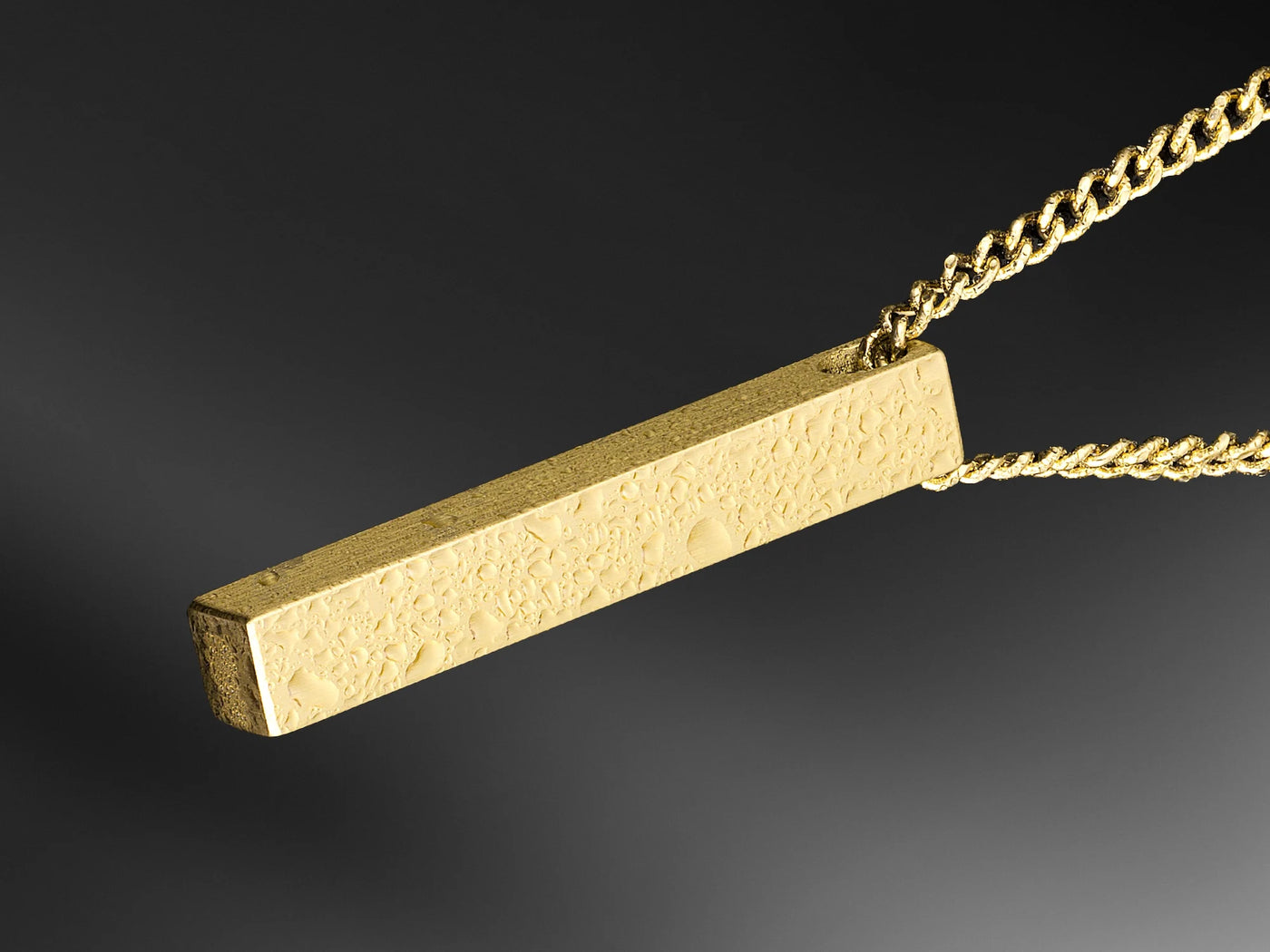 Gold bar pendant on a chain against a dark background
