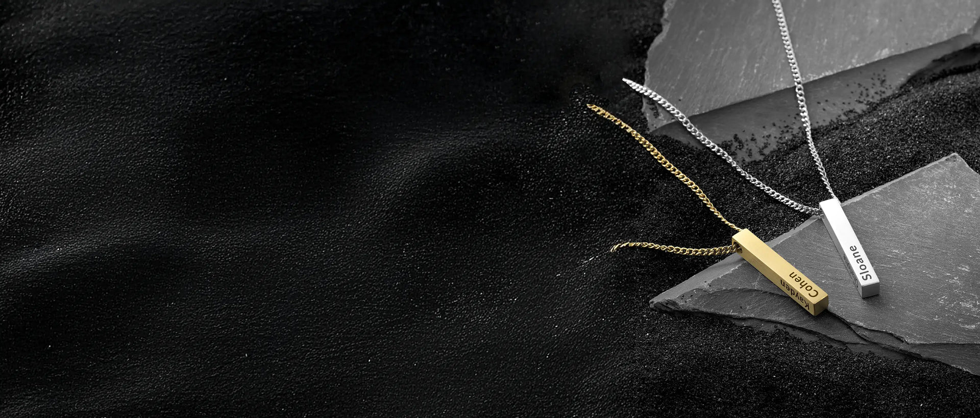 Two necklaces with engraved pendants on a dark stone surface