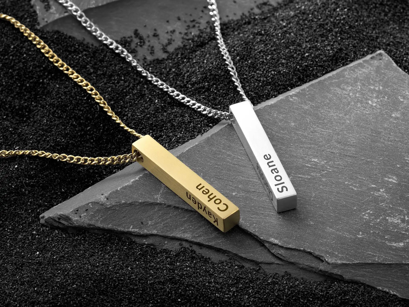 Two necklaces with horizontal pendants on a dark stone surface