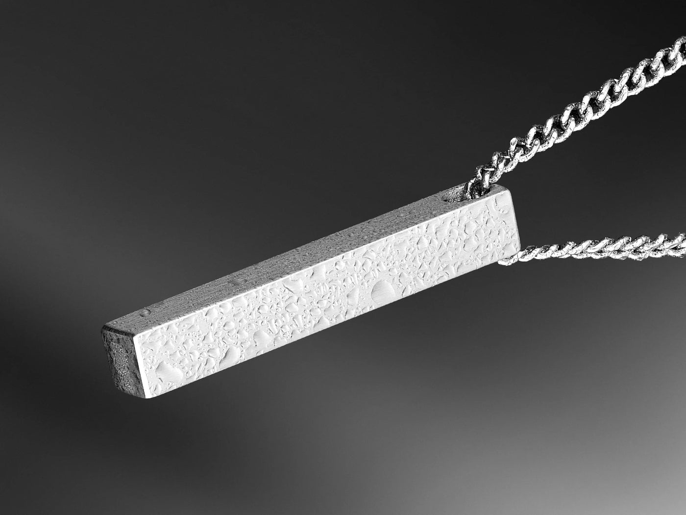 Silver pendant on a chain against a dark background