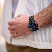 Person wearing a black watch with a detailed face on a blurred background