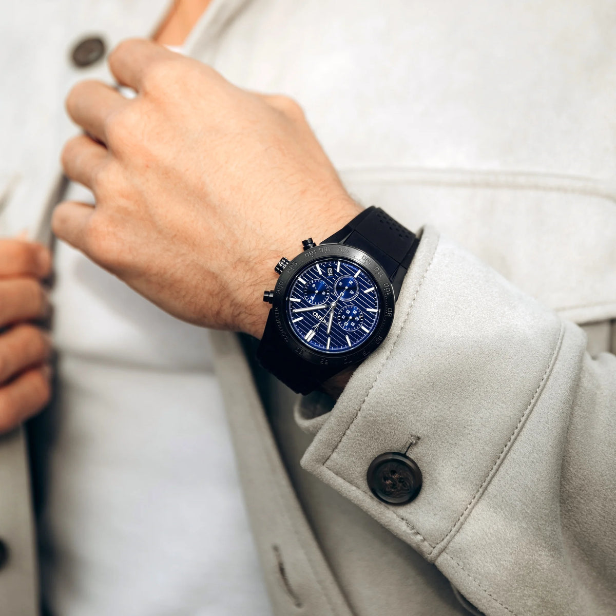 Hand wearing a black watch with a blue face, close-up of wrist and coat.