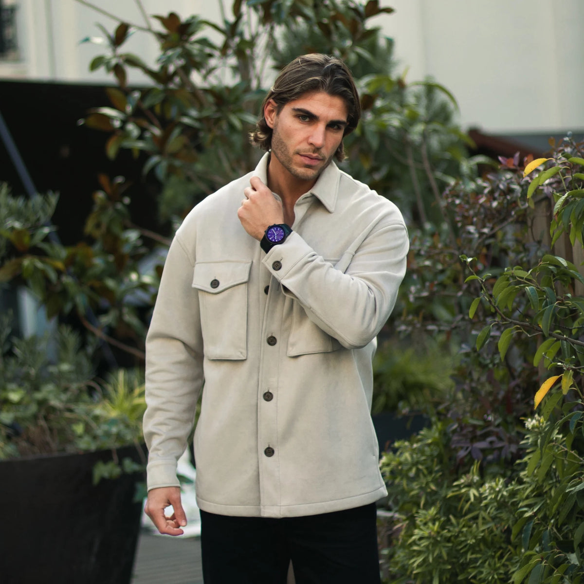 Man wearing a beige jacket with plants in the background