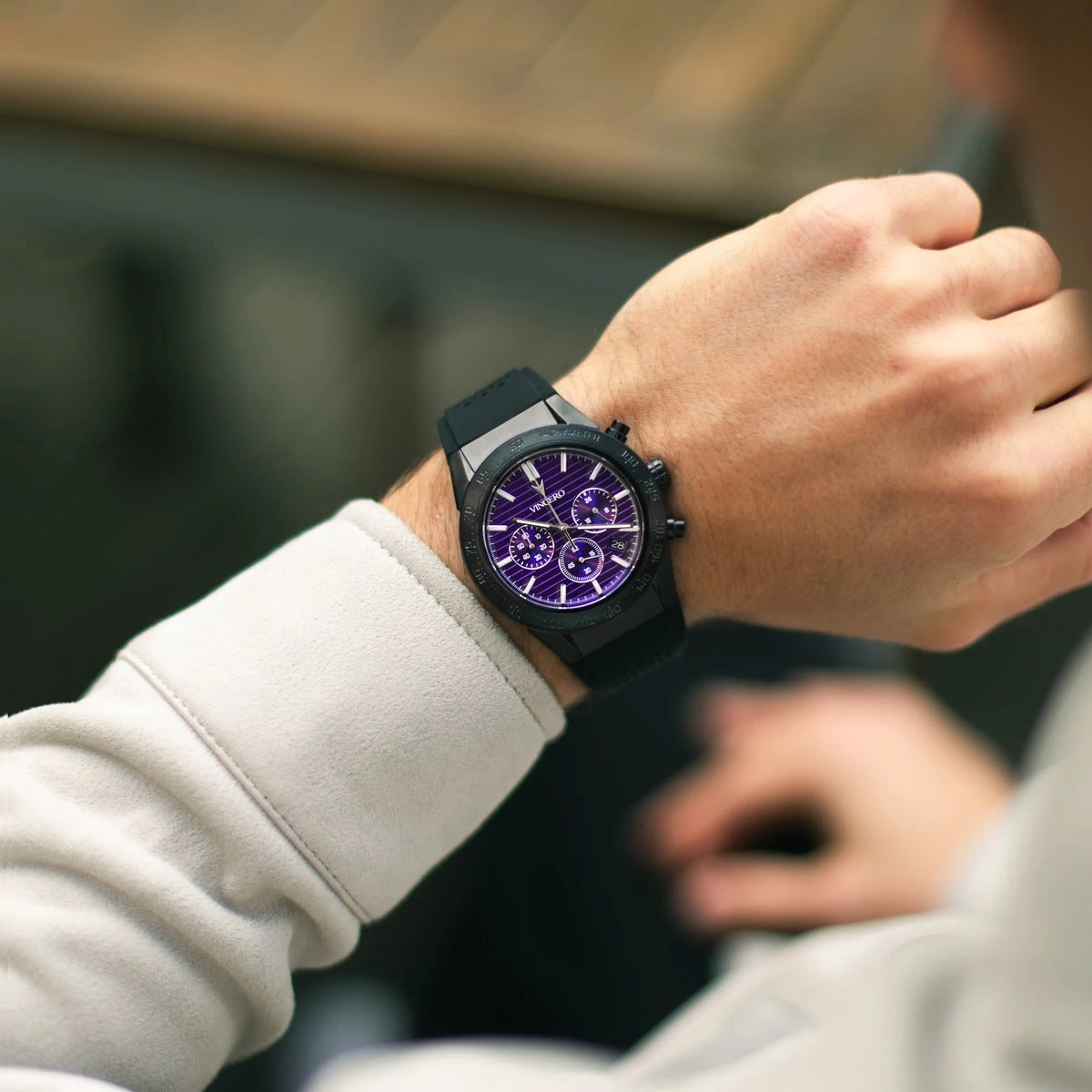 Person wearing a black watch with a purple face on a blurred background