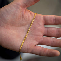 Gold rope chain on a hand against a neutral background