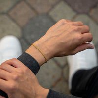Close-up of a person's wrist wearing a gold bracelet with a blurred background.