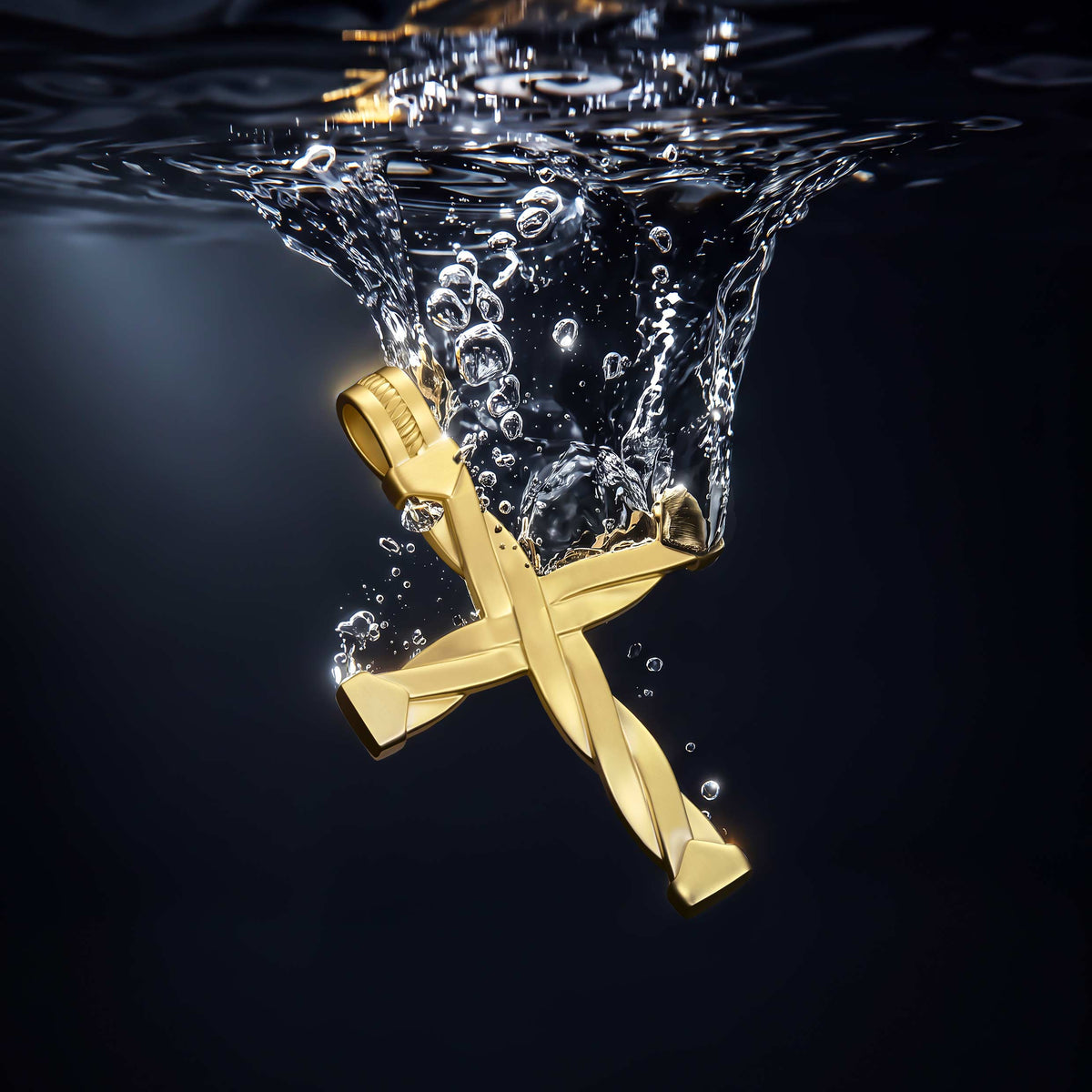 A gold cross pendant with a twisted central design, shown plunging underwater with a dramatic splash of water and bubbles at the surface against a dark background.
