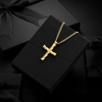 A gold cross pendant necklace on a gold chain, displayed on a black gift box with the brand name VINCENZO partially visible, surrounded by black gift packaging and satin bows.