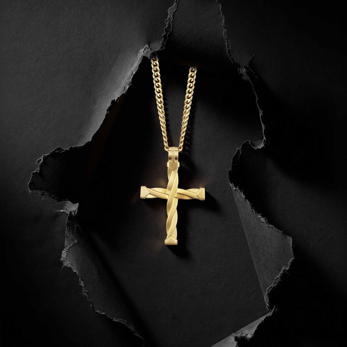 A gold cross pendant with a twisted rope design hangs from a matching gold chain against a dark textured background with torn paper effect.