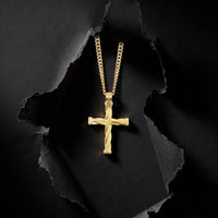A gold cross pendant with a twisted rope design hangs from a matching gold chain against a dark textured background with torn paper effect.